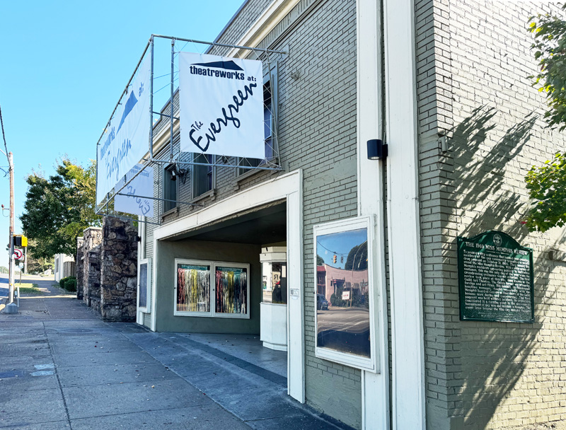 Brick building withmodeled trim holds the entrance to a theatre with a circular box office booth outside the entryway doors.  Sign above the entry proclaims it to be 