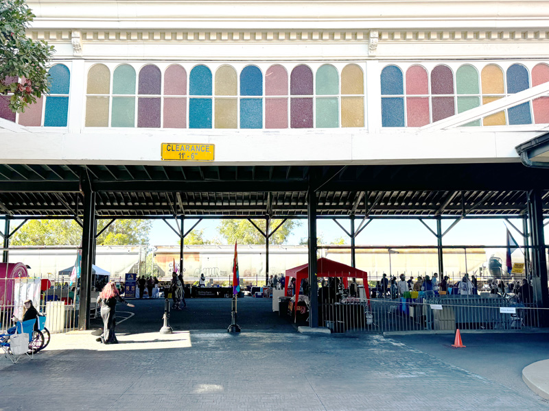 Beneath what appears to be an elevated train line or walkway vendors set up booths on a concrete mall.