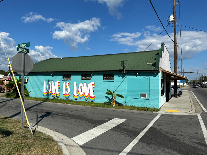 Side view of a cinderblock building. The walls are painted bright blue and a mural of the words 