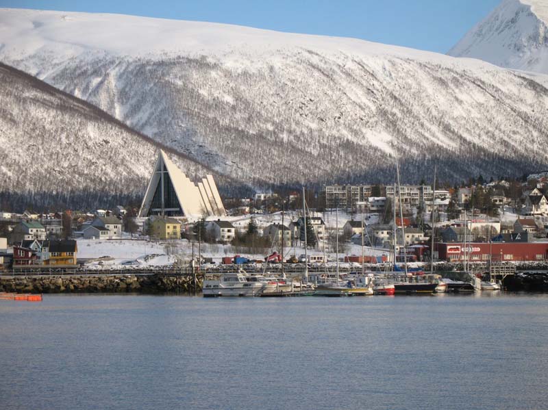 A tall building rises above surrounding town with receding triangular roofs of that grow smaller toward the center and then larger again in the rear