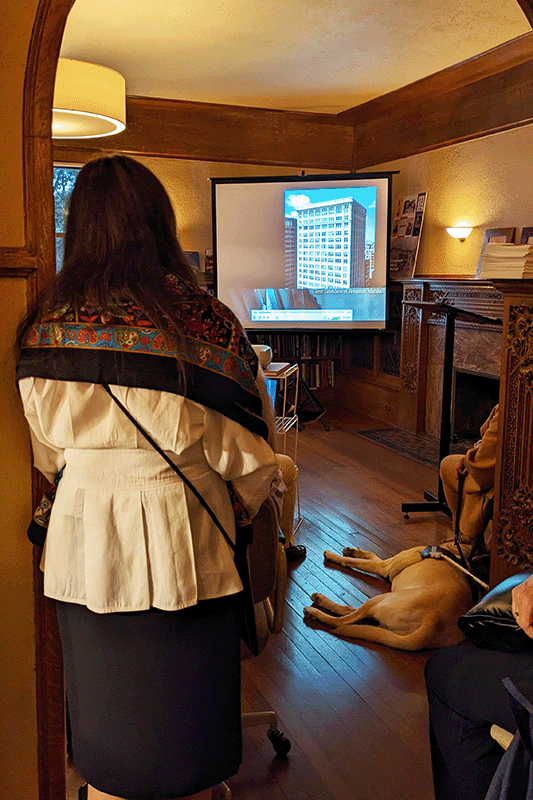 Woman stands in arched doorway facing a projector screen. On the screen is an image of a skyscraper in the Chicago skyline.