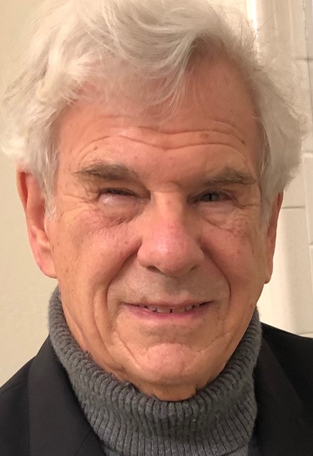 Headshot image of Stephen Tobriner, a white man with short white hair wearing a grey turtleneck sweater and black jacket.