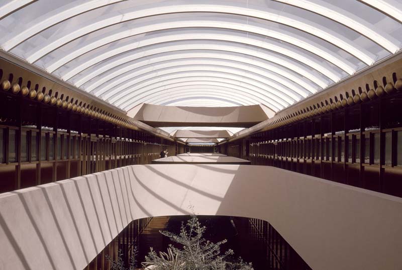 Spacious atrium with a curved glass ceiling allowing natural light. First floor is open to the second, bridged by several traverses. The space features geometric design elements and symmetrical corridors.