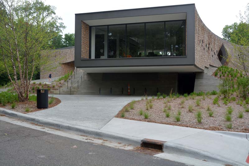 A modern building with a cantilevered glass facade, curved stone walls, and integrated landscaping, featuring stairways and a minimalist design.