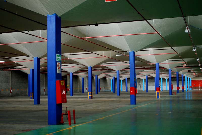 expansive industrial space with concrete floors and walls with blue pillars and red beams overhead